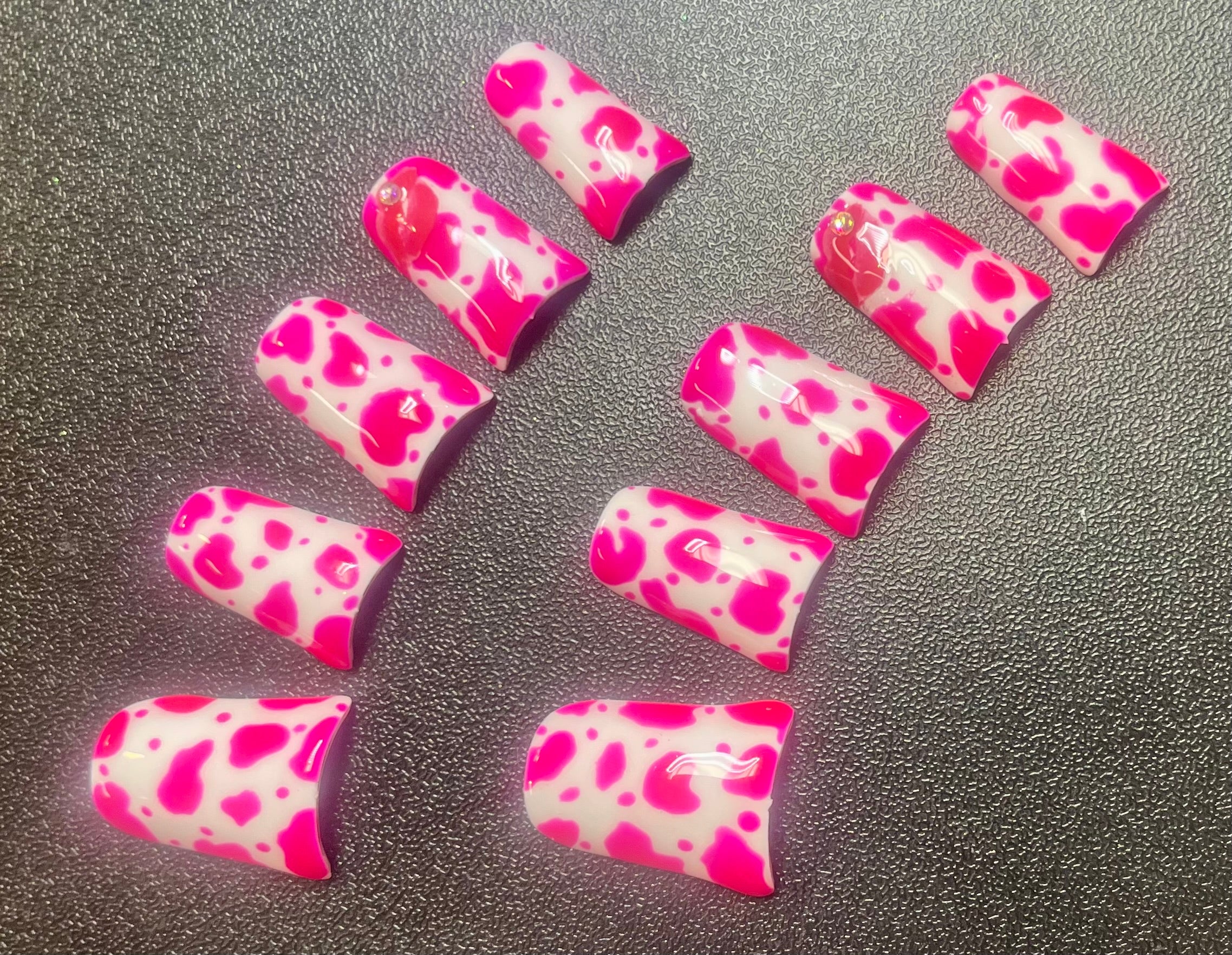 Pink and white patterned nail art pieces on a dark surface